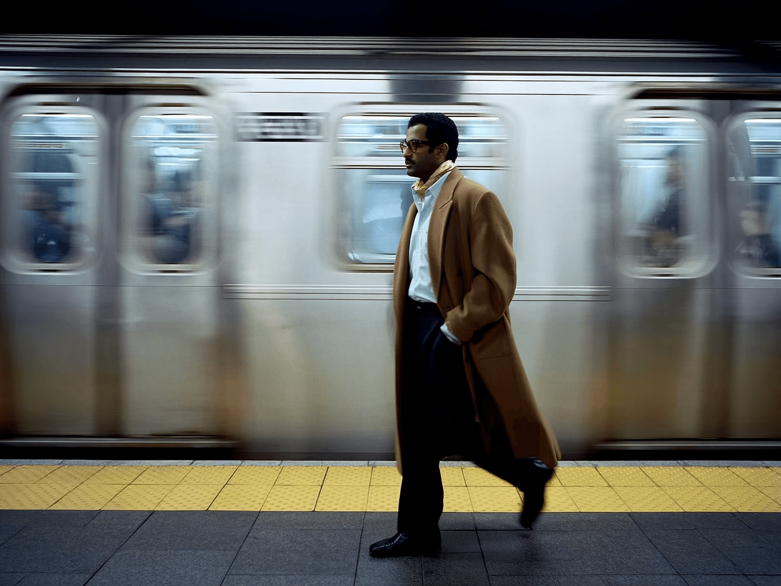 AI-generated Instagram ad creative — editorial fashion shot of man in camel overcoat walking confidently past blurred subway train, urban high-fashion image generated by FastiAds